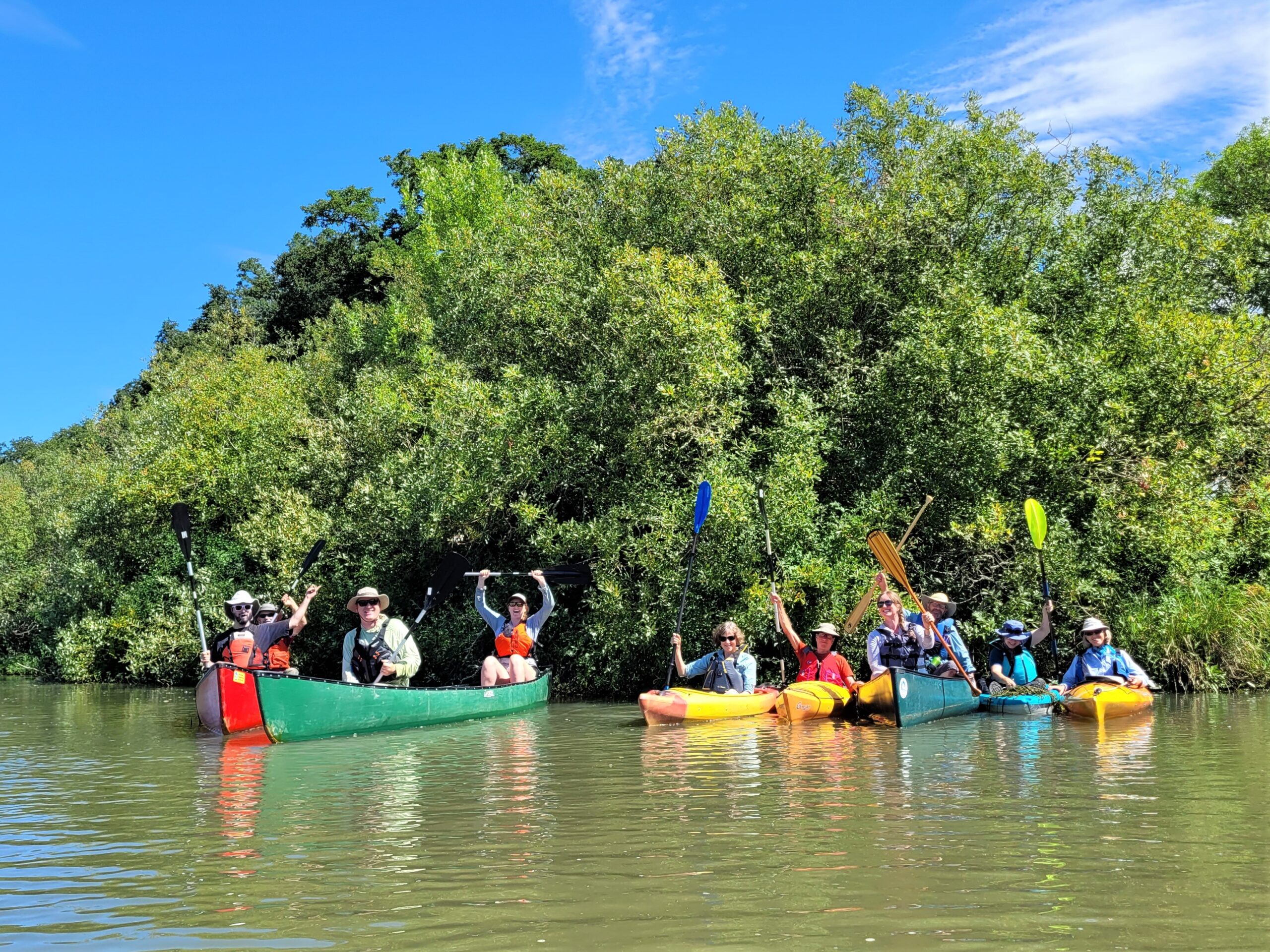 A group of kayakers raise their paddles in a celebratory gesture